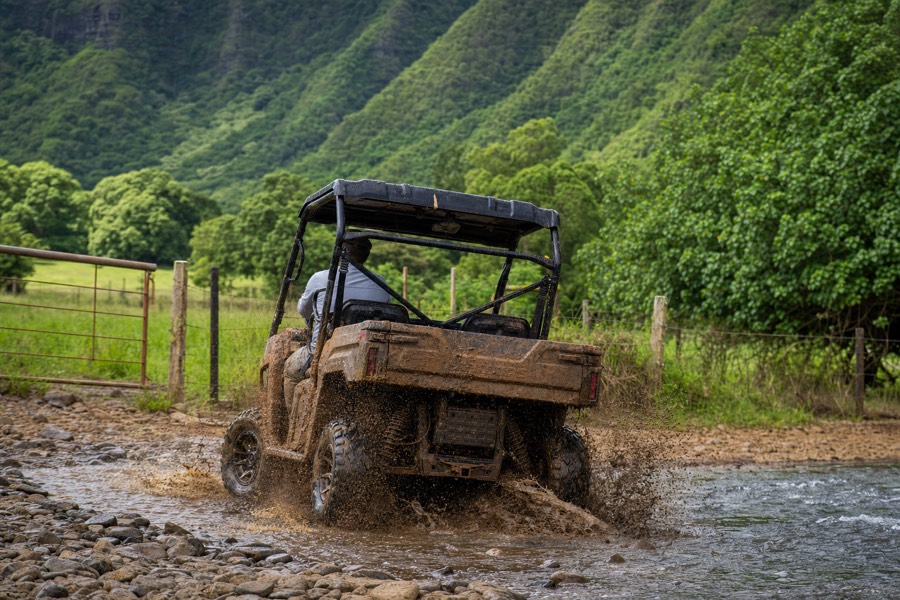 A mud-splattered off-road vehicle crossing a stream on Kipu Ranch, Kauai