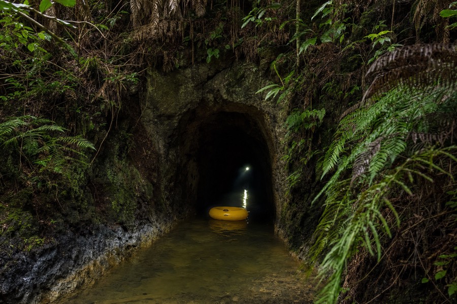 The dark mouth of a historic hand-dug irrigation tunnel in Kauai jungle with an inner tube floating at the entrance