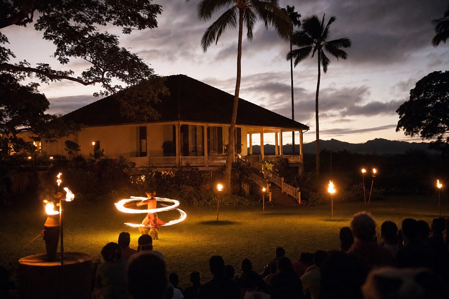 A torch-lit luau stage at dusk on a historic Kauai plantation with a fire dancer