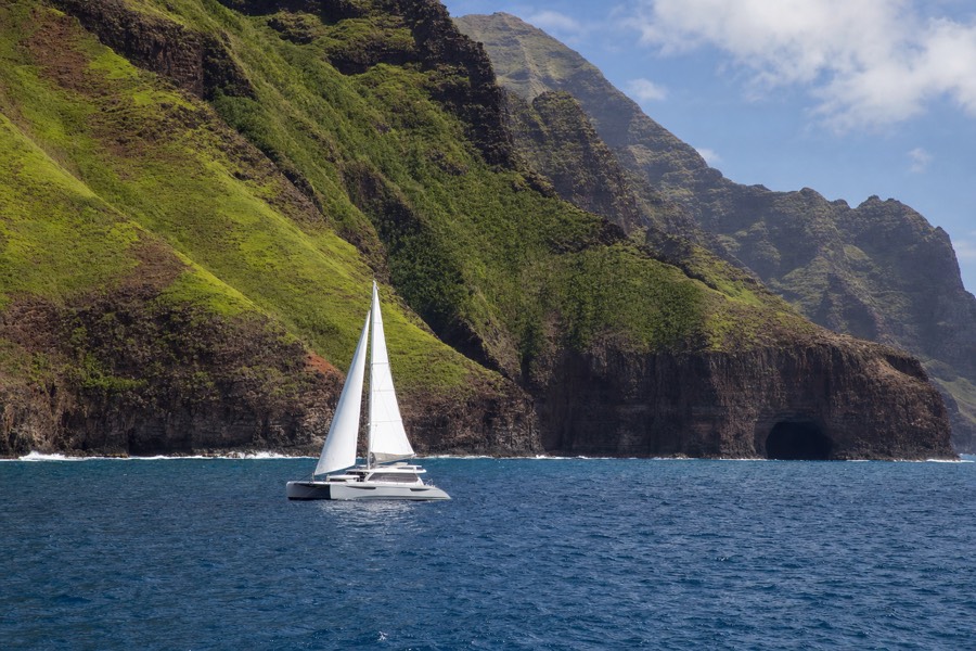 A sailing catamaran with sails up along the Na Pali Coast cliffs on Kauai