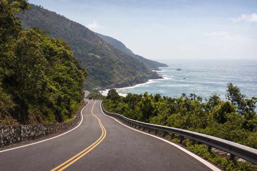 Kauai's coastal highway curving between green hills with a single lane of traffic and no shoulder development
