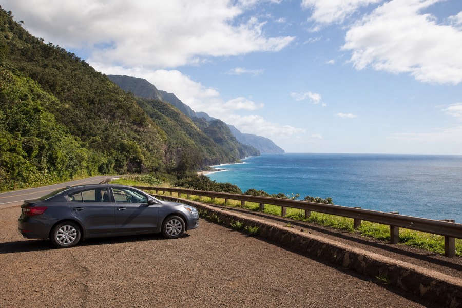 Rental car parked at a scenic roadside pull-off on Kauai with the coastline stretching beyond it