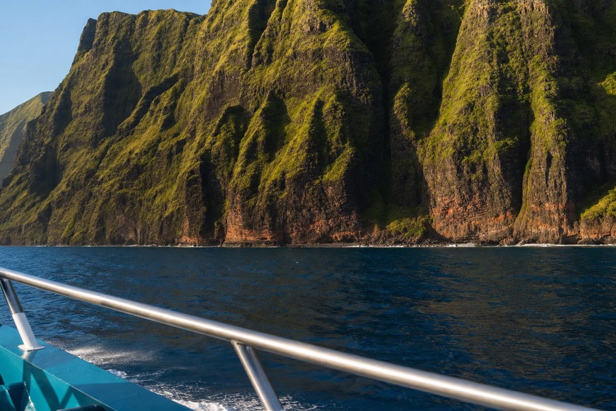 Tour boat deck view looking toward the fluted green sea cliffs of the Na Pali Coast in late afternoon light