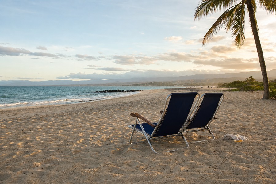 A quiet, nearly empty south-shore Kauai beach in late afternoon light with folding chairs and no crowds